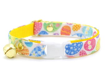 May include: A yellow and white cat collar with a bell. The collar is decorated with a colorful Easter egg pattern.