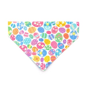 May include: White dog bandana with a colorful Easter egg pattern. The eggs are decorated with different colors and designs.
