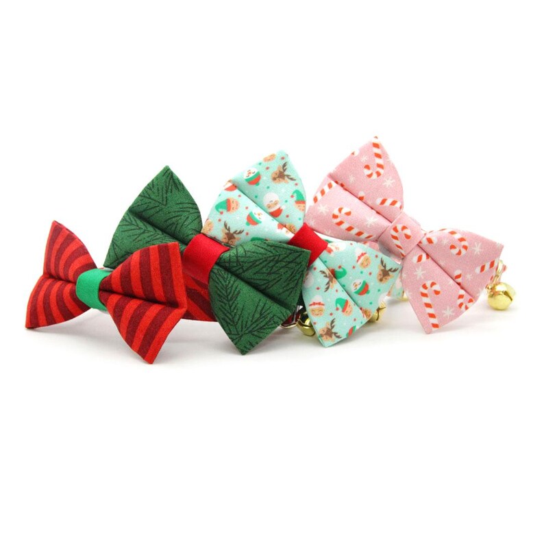 May include: Four festive Christmas-themed bow ties for pets. The bow ties are made of fabric and feature different patterns, including candy canes, snowflakes, and Christmas trees. The bow ties are attached to a bell.