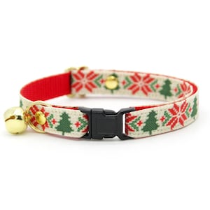 May include: A festive cat collar with a Christmas tree and snowflake pattern in red, green, and white. The collar has a gold bell and a black plastic buckle. The inner lining is red.