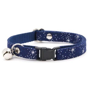 Puede incluir: Un collar para mascota de color azul oscuro con un patrón de estrellas y destellos blancos. Incluye una hebilla de plástico negro, una anilla en D de metal plateado, un pequeño cascabel plateado y un remache de metal plateado para ajuste.