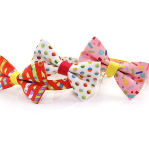 May include: Three colorful bow ties with different patterns. The bow ties are made of fabric and have a yellow elastic band. The patterns include candles, confetti, and polka dots.