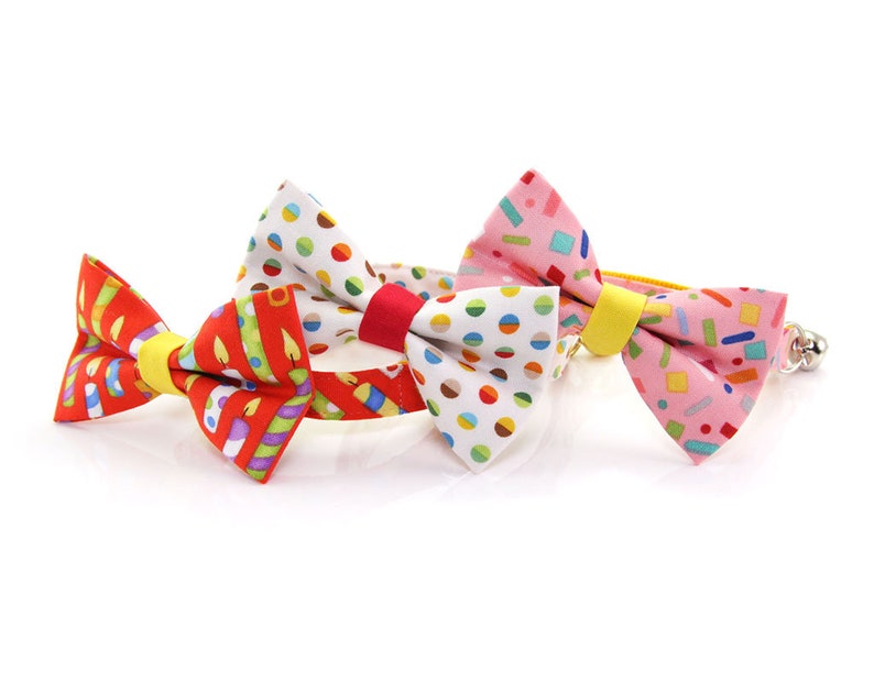 May include: Three colorful bow ties with different patterns. The bow ties are made of fabric and have a yellow elastic band. The patterns include candles, confetti, and polka dots.
