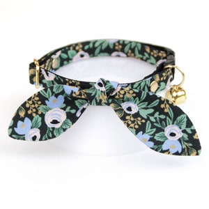 May include: A black cat collar with a floral pattern in shades of blue, green, and gold. The collar has a bow tie and a bell.