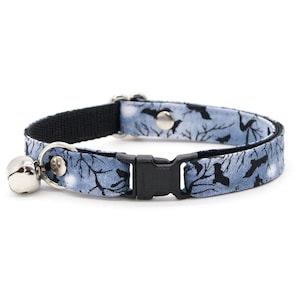 Op de afbeelding: Een huisdierhalsband met een lichtblauwe stoffen overlay met een patroon van zwarte silhouetten van vleermuizen en kale boomtakken tegen een maanverlichte lucht. De halsband is voorzien van een zwarte plastic gesp en een zilveren belletje.