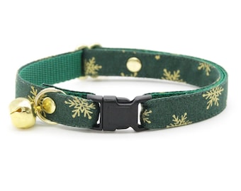 May include: A green cat collar with a gold snowflake pattern and a gold bell. The collar has a black plastic buckle and a gold-colored metal loop for the bell. The collar is approximately 0.5 inches wide.