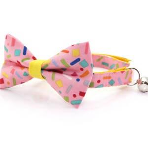 May include: Pink cat collar with a colorful confetti pattern bow tie and a silver bell.