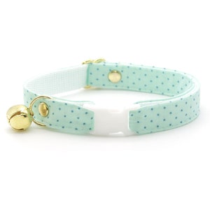 May include: A light blue cat collar with white polka dots and a gold bell. The collar has a white plastic buckle.