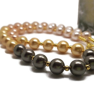 Peut inclure: Un collier de perles multicolores présentant un dégradé de perles sphériques dans des tons gris foncé, or métallique et rose tendre. Les perles sont séparées par de petites entretoises en métal doré poli, formant un cercle continu.