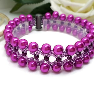 May include: A magenta beaded bracelet with a double-strand design. The bracelet features large, round beads and smaller accent beads, connected by a delicate, openwork pattern. The clasp is a silver-tone magnetic closure.