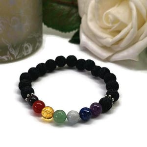 May include: A black lava stone bracelet featuring seven chakra beads in various colours. The chakra beads are red, orange, yellow, green, light blue, dark blue, and purple. The bracelet is on a white surface.