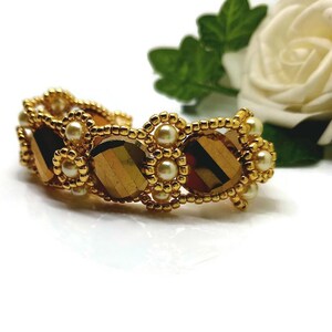 May include: A gold bracelet featuring brown and gold beads with white pearl accents.