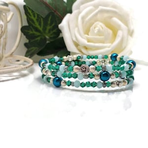 May include: A multi-strand bracelet with teal, green, and silver beads. The bracelet features a mix of faceted and round beads, with a silver flower charm. The design is coiled, creating a layered effect.