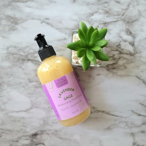 May include: A clear plastic bottle of yellow liquid hand soap with a black pump dispenser. The label is purple with white text reading Olive Blossom Soap Co., Lavender Sage, Moisturizing Hand Soap, Olive Oil + Dead Sea Salt, 8 Fl Oz.