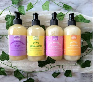 May include: Four clear plastic pump bottles of Olive Blossom Soap Co. moisturizing hand soap, each containing 8 fl oz. The labels are purple, yellow, pink, and orange, featuring scents French Lavender & Honey, Citrus Lemongrass, Black Raspberry Vanilla, and Orange Blossom.