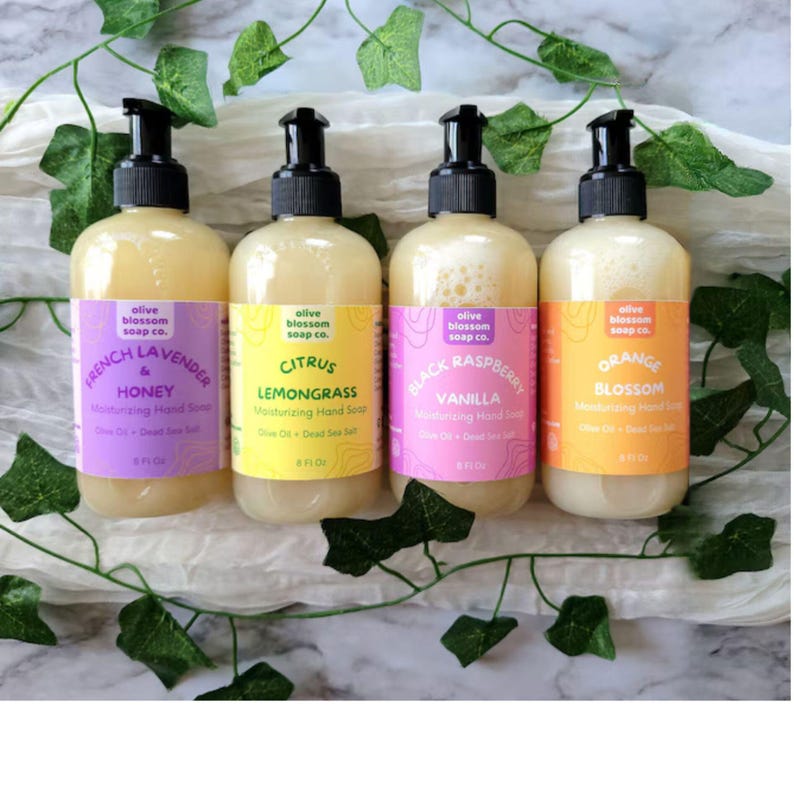 May include: Four clear plastic pump bottles of Olive Blossom Soap Co. moisturizing hand soap, each containing 8 fl oz. The labels are purple, yellow, pink, and orange, featuring scents French Lavender & Honey, Citrus Lemongrass, Black Raspberry Vanilla, and Orange Blossom.