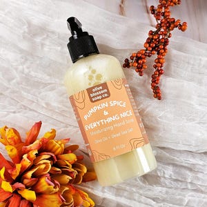 May include: A clear plastic bottle of Pumpkin Spice & Everything Nice moisturizing hand soap with a black pump dispenser. The label features the text Olive Blossom Soap Co., Pumpkin Spice & Everything Nice, Moisturizing Hand Soap, Olive Oil + Dead Sea Salt, and 8 Fl Oz.