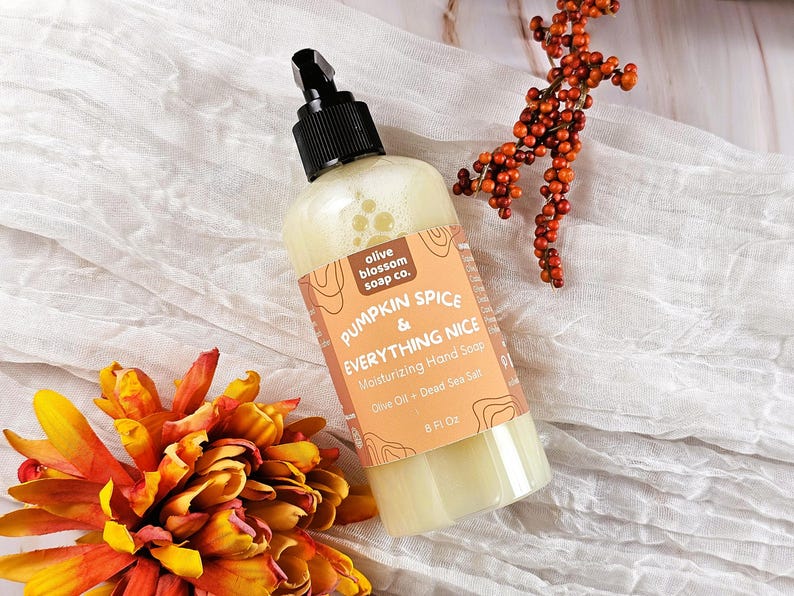 May include: A clear plastic bottle of Pumpkin Spice & Everything Nice moisturizing hand soap with a black pump dispenser. The label features the text Olive Blossom Soap Co., Pumpkin Spice & Everything Nice, Moisturizing Hand Soap, Olive Oil + Dead Sea Salt, and 8 Fl Oz.