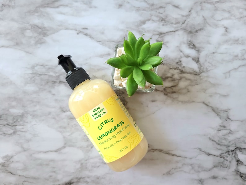 May include: A clear plastic bottle of yellow Citrus Lemongrass moisturizing hand soap with a black pump dispenser. The label reads Olive Blossom Soap Co., Citrus Lemongrass, Moisturizing Hand Soap, Olive Oil + Dead Sea Salt, 8 Fl Oz.