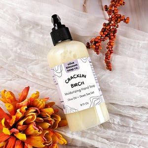 May include: A clear plastic bottle of Cracklin Birch moisturizing hand soap with a black pump dispenser. The label features the text olive blossom soap co., Cracklin Birch, Moisturizing Hand Soap, Olive Oil + Dead Sea Salt, and 8 Fl Oz.