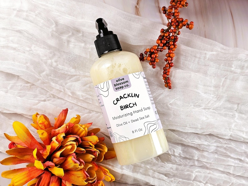 May include: A clear plastic bottle of Cracklin Birch moisturizing hand soap with a black pump dispenser. The label features the text olive blossom soap co., Cracklin Birch, Moisturizing Hand Soap, Olive Oil + Dead Sea Salt, and 8 Fl Oz.