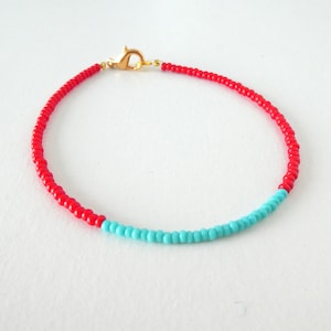 May include: A red and turquoise beaded bracelet with a gold clasp.