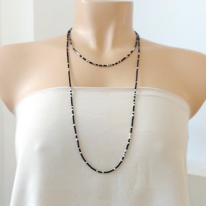 May include: A layered necklace with black and white beads. The necklace is made of small, round beads that are strung together in a simple pattern. The necklace is long and hangs down to the chest.