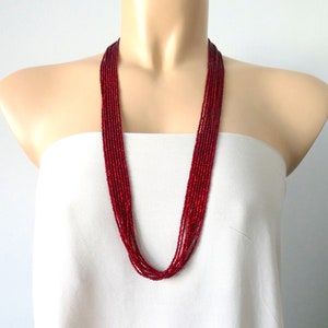 May include: A long red beaded necklace made of small, round beads. The necklace is layered and hangs down to the chest.