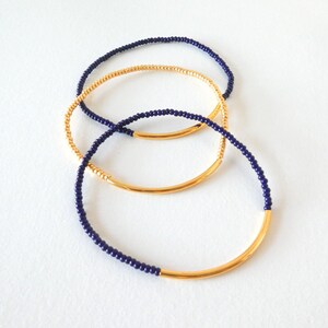 May include: Three gold and navy blue beaded bracelets stacked on top of each other. The bracelets are made of small beads and have a gold metal band.