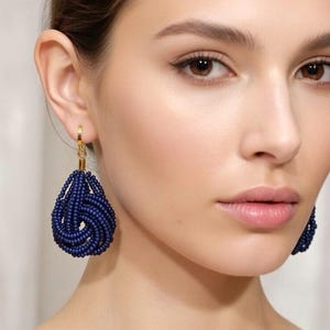 Peut inclure: Boucles d'oreilles en perles bleu marine avec crochets dorés. Les boucles d'oreilles ont une forme de goutte d'eau, avec les perles finement tissées ensemble. Les boucles d'oreilles sont de couleur bleu foncé et semblent légères.