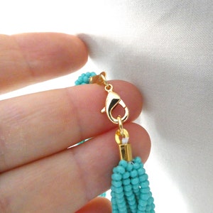 May include: A turquoise blue beaded necklace with a gold clasp. The necklace is made of multiple strands of small beads.