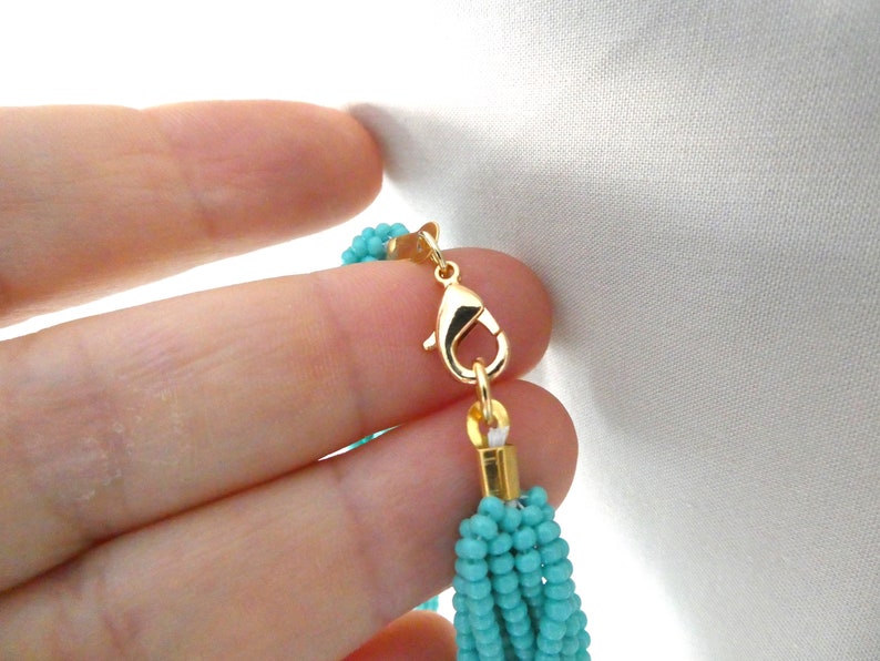 May include: A turquoise blue beaded necklace with a gold clasp. The necklace is made of multiple strands of small beads.