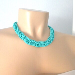 May include: A turquoise blue braided necklace made of small beads. The necklace is on a mannequin's neck.