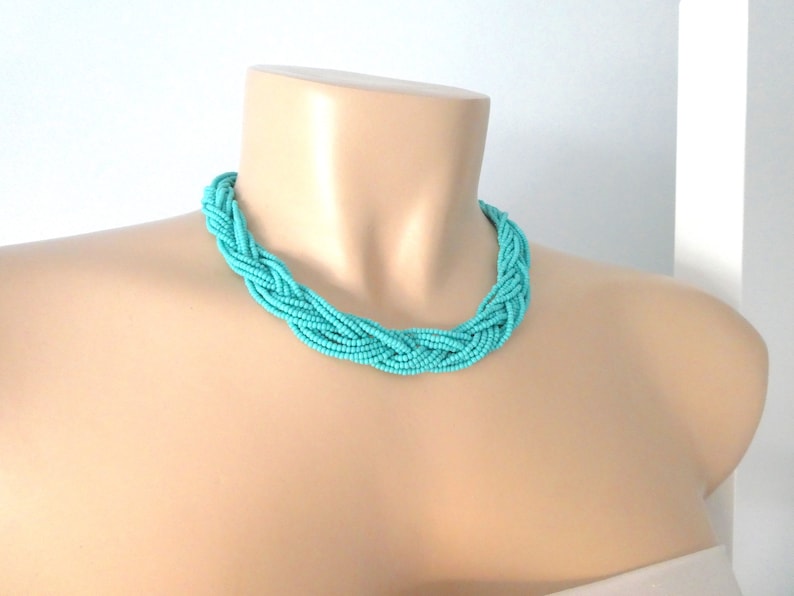 May include: A turquoise blue braided necklace made of small beads. The necklace is on a mannequin's neck.