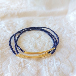 May include: A navy blue beaded bracelet with two gold metal bars.