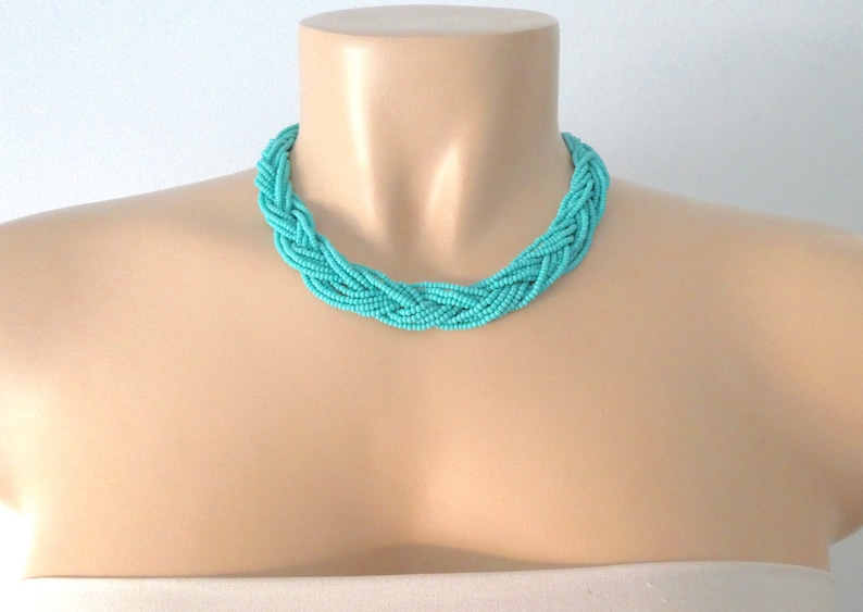 May include: A turquoise blue braided necklace made of small seed beads. The necklace is on a mannequin's neck.