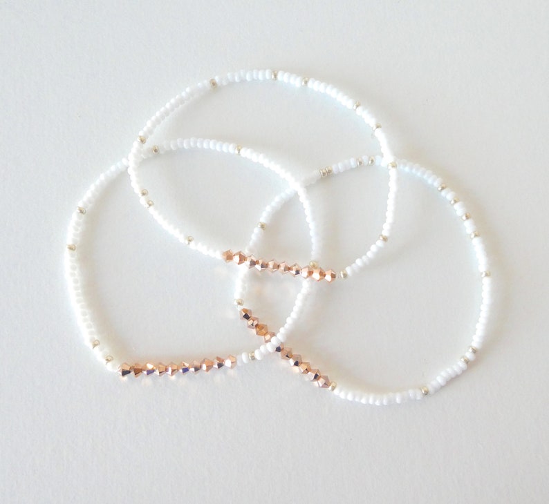May include: Three delicate bracelets. Each bracelet features small white beads and silver accents. One section of each bracelet is adorned with rose gold-colored faceted beads. The bracelets are arranged in a circular pattern against a white background.