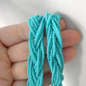 May include: A strand of turquoise blue seed beads, braided together in a rope-like shape.