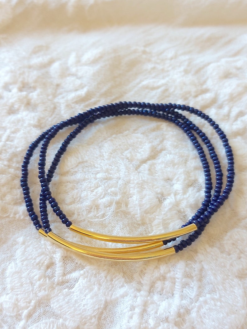 May include: A triple-strand bracelet made of dark blue beads with a gold bar accent.