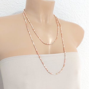 May include: A layered necklace with small, white, pink, and gold beads. The necklace is on a mannequin.