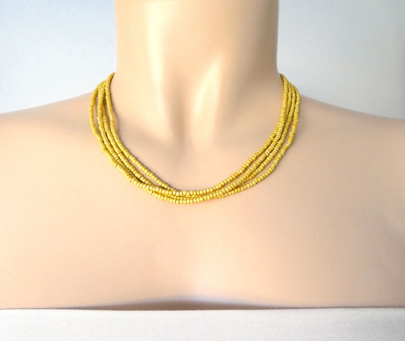 May include: A multi-strand necklace made of small, matte gold beads. The necklace is layered and has a simple, elegant design.
