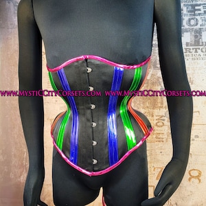 Può includere: Un corsetto nero con un designo a righe rosa, blu, verde e arancione. Il corsetto ha una chiusura a busk nella parte anteriore ed è realizzato in un tessuto simile al raso.