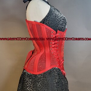 May include: A red corset with a mesh design and a lace-up back. The corset is made of a satin-like fabric and has a boned structure. The corset is shown on a mannequin and has the website address "www.mysticcitycorsets.com" printed on the bottom.