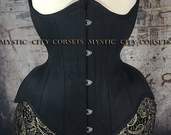 Può includere: Un corsetto nero dal design strutturato, con una fila di bottoni sul davanti. Il corsetto è esposto su un manichino. Il bordo inferiore è rifinito con pizzo dorato. Il testo "MYSTIC CITY CORSETS" è visibile.