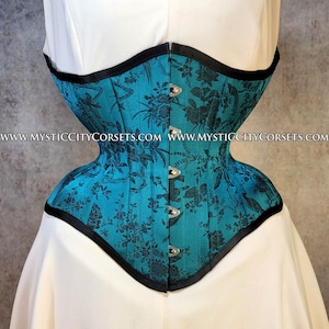 May include: Teal corset with a black floral pattern. The corset has a structured design with a black trim and silver clasps. The corset is displayed on a white background.