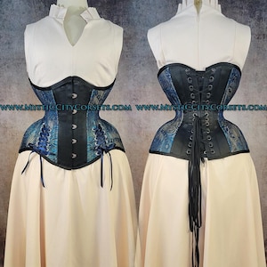 May include: A corset featuring a blue and black peacock feather pattern with solid black panels, front busk closures, side lacing with ribbons, and back grommet lacing with long black cords. The text WWW.MYSTICCITYCORSETS.COM is visible.