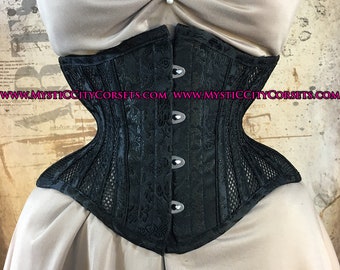 Può includere: Corsetto nero con motivo floreale e pannelli in rete. Il corsetto ha una chiusura a busk in acciaio ed è realizzato in tessuto satinato. Il corsetto è mostrato su un manichino con una gonna marrone chiaro.