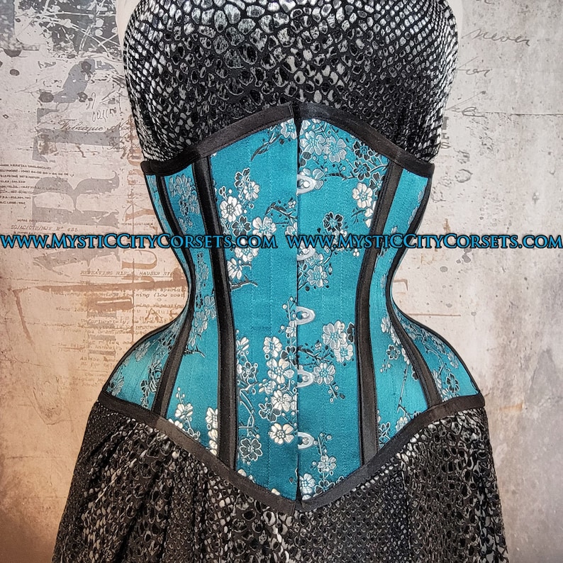May include: A turquoise blue corset with black boning and a floral pattern. The corset has a satin finish and is made of high-quality materials. www.mysticcitycorsets.com
