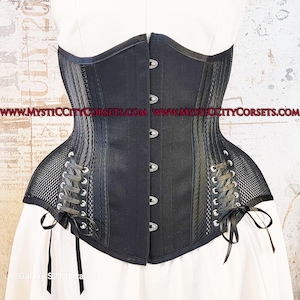 May include: Black corset with a structured design. The corset features a central panel with silver clasps, side panels with a mesh overlay, and lace-up detailing. The garment has a curved silhouette and is displayed against a white background.