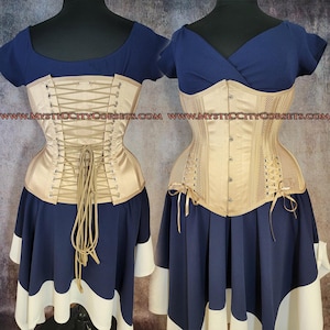 Può includere: Due manichini mostrano un abito con corsetto. L'abito presenta un corsetto beige con schiena allacciata, abbinato a una gonna blu navy e finiture bianche. La parte superiore è blu navy, a maniche corte. L'indirizzo del sito web è visibile in alto.